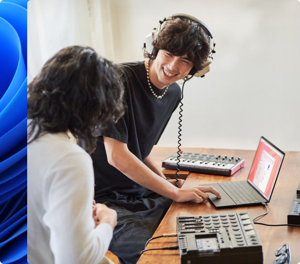 Ein lächelnder junger Mann mit Kopfhörern und eine andere Person, die mit einem elektronischen Keyboard Musik auf einem Laptop macht