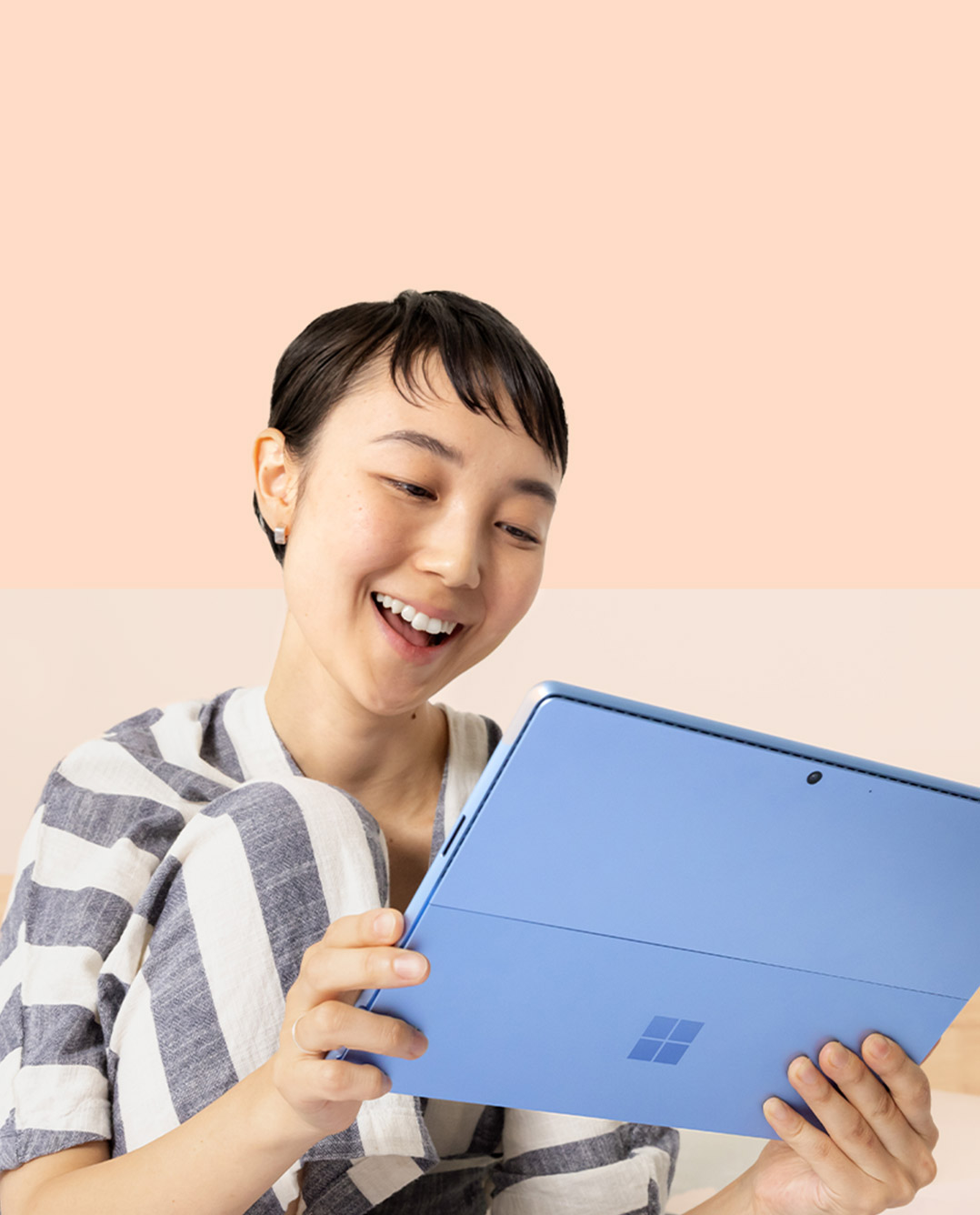 امرأة تبتسم وهي تستخدم لابتوب Surface Pro 9 باللون أزرق ياقوتي، وتُمسِك بقلم Surface Slim Pen 2.