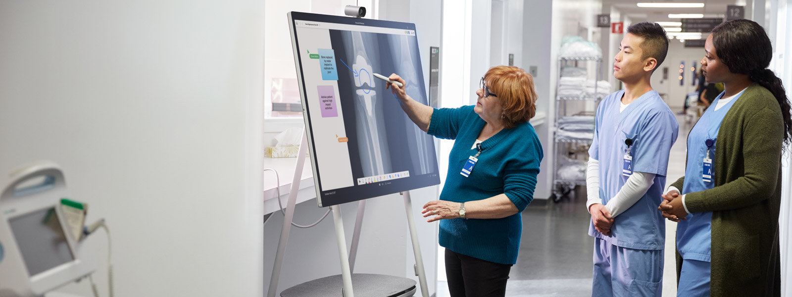 A woman interacts with the screen of a Surface Hub 2S while two people observe