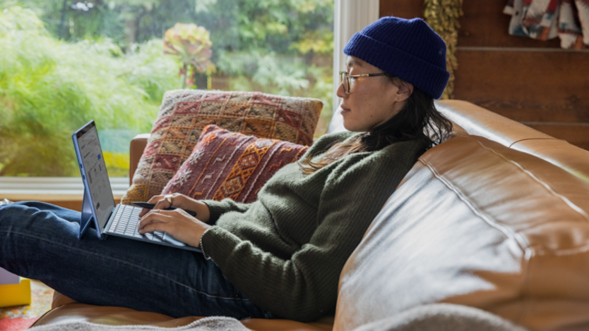 A woman sitting on a couch works on her Surface device