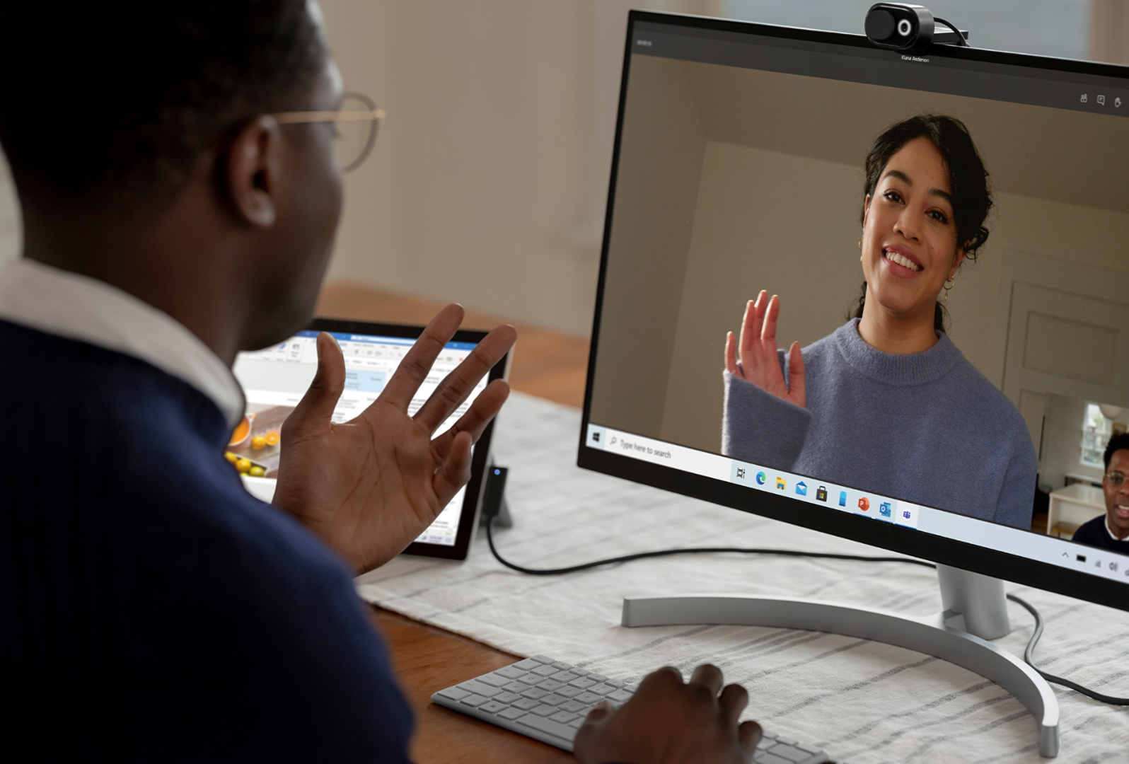 Een man gebruikt zijn Surface-apparaat aangesloten op een externe monitor en Microsoft Modern Webcam om een collega te spreken in een gesprek in Microsoft Teams
