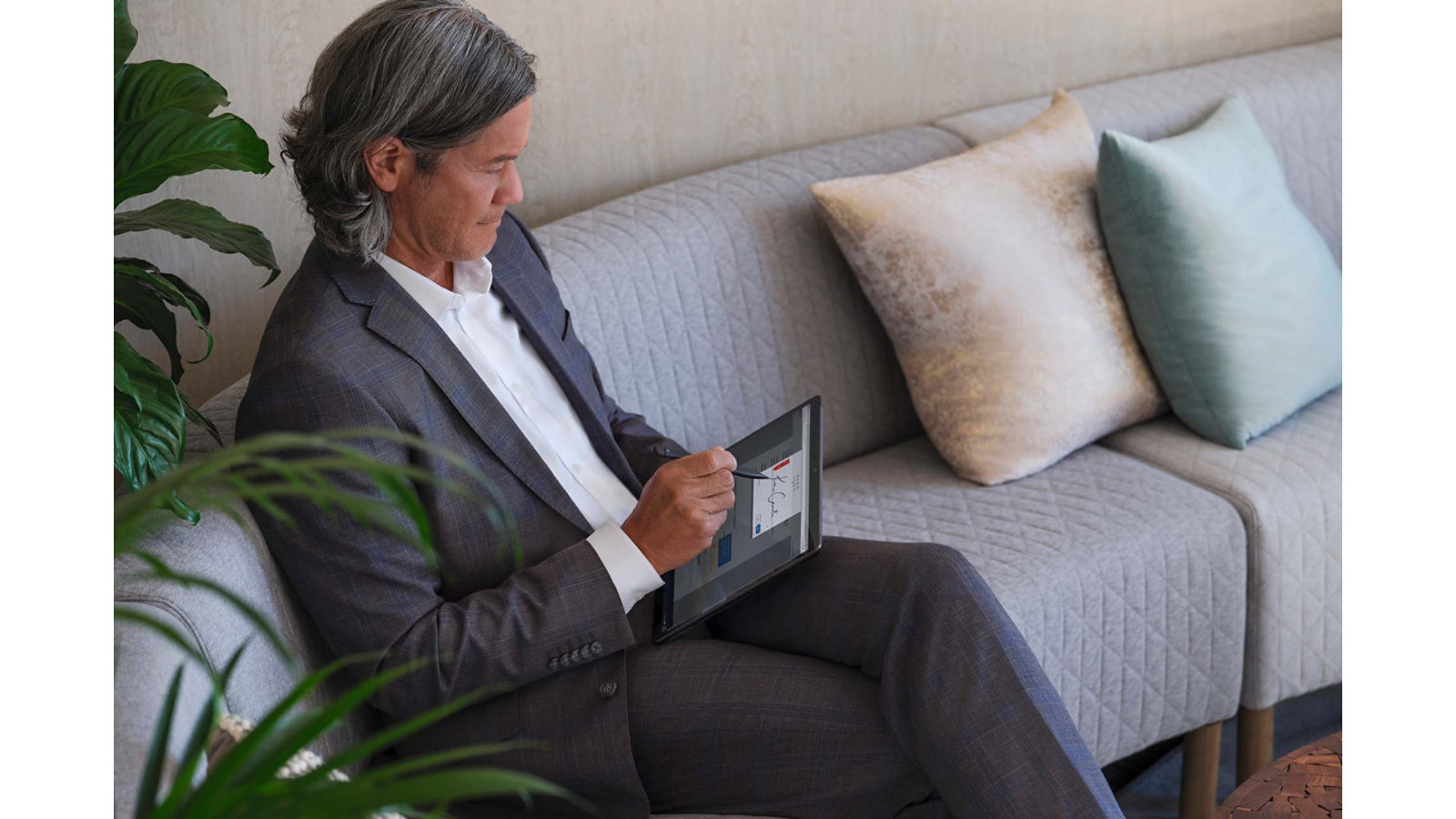 A person writes with Surface Slim Pen 2 on Surface Pro 8 while seated on a sofa in an office lobby