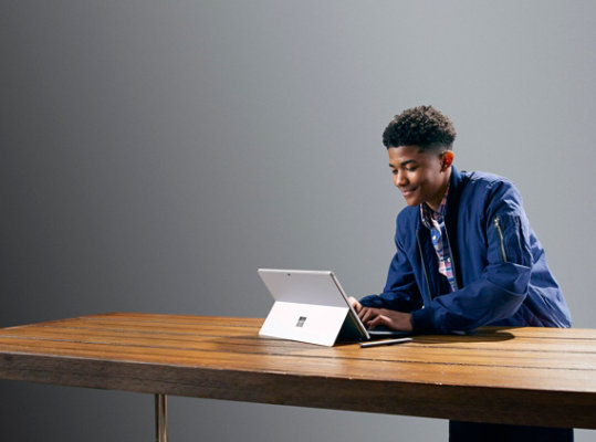 رجل يستخدم جهاز Surface Pro 7 مع غطاء الكتابة Type Cover أثناء جلوسه على طاولة.