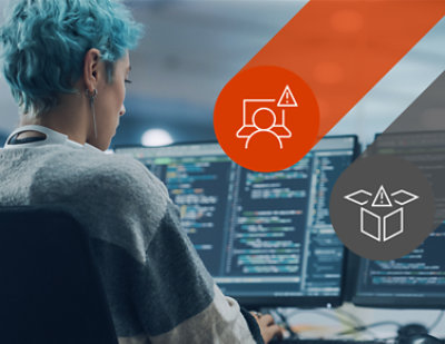 Una mujer está sentada frente a un ordenador con dos monitores delante.