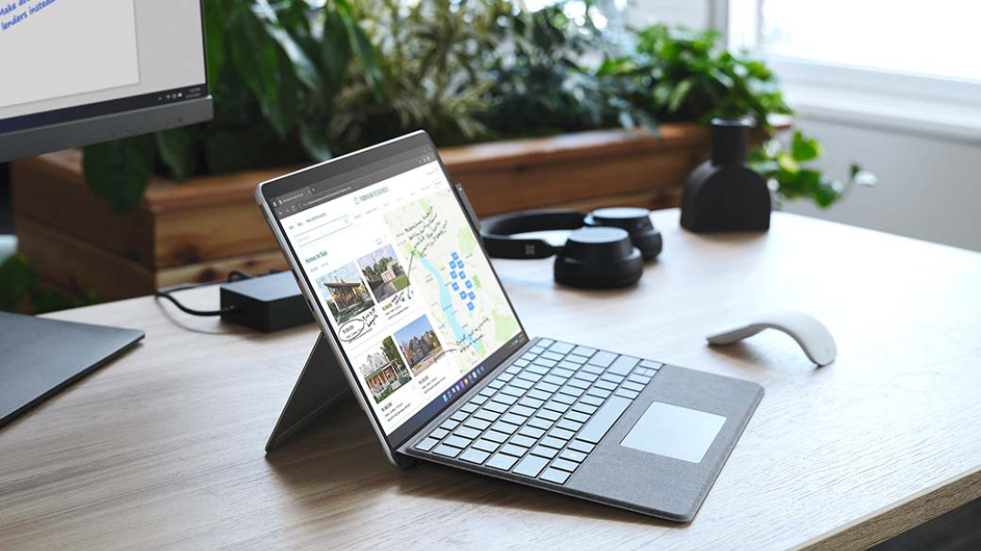 Surface Pro X på skrivebord i kontoromgivelser ved siden av flere Surface-tilbehørsenheter