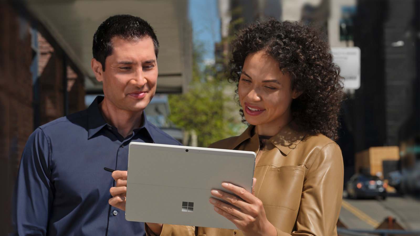 Zwei Personen stehen auf einem Bürgersteig in einer großen Stadt und betrachten den Bildschirm ihres Surface Pro X im Tablet-Modus
