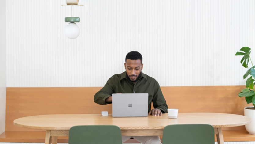 A man sitting at a table with a Surface Laptop 5 and Surface Arc Mouse