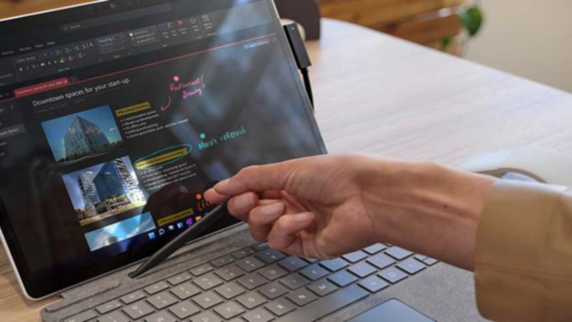 A person's hand is observed placing Surface Slim Pen 2 into the built-in storage inside Surface Pro Signature Keyboard