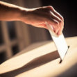 A hand placing a piece of paper into a slot, symbolizing voting or ballot submission.