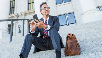 A person sitting on the steps outside of a building using a mobile phone.