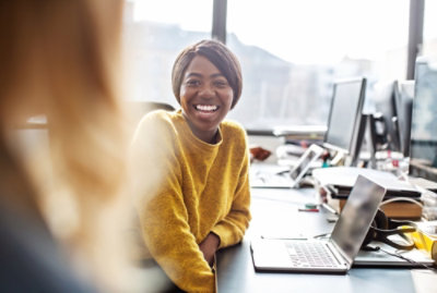A women sitting next to her laptop and smiling.