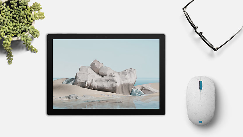 A Ocean Plastic Mouse next to a Surface device in tablet mode with reading glasses and a plant nearby. 
