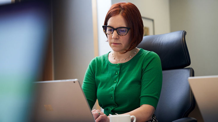 A lady in a green shirt and glasses sitting in a chair using a laptop