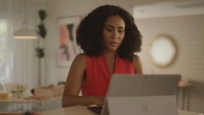 Eine Frau, die am Laptop arbeitet und dabei an einem Tisch sitzt