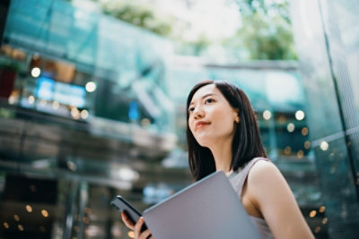 Woman holding laptop and mobile device in an office building.