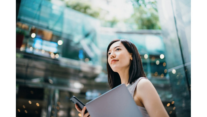 Woman holding laptop and mobile device in an office building.