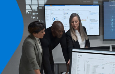 Three people working together in a room with many screens displaying data.