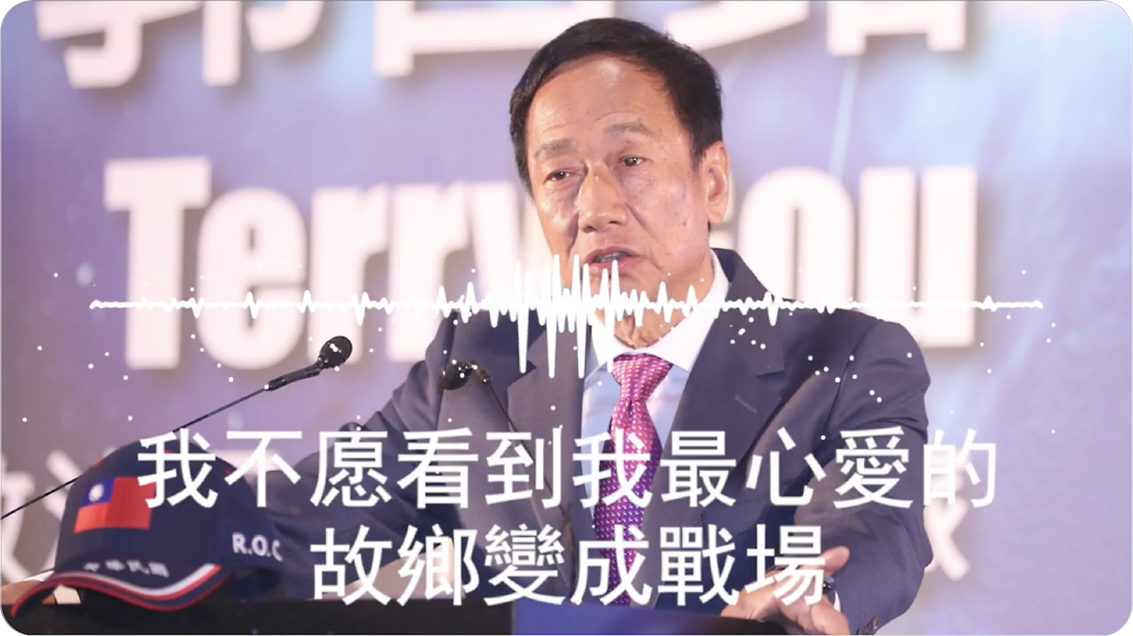 A man in a suit speaking at a podium with chinese text and a graphic of an audio waveform in the foreground.