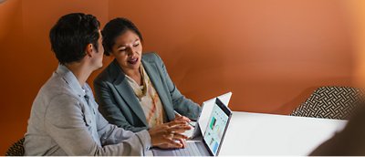 Twee zakenmensen die aan een tafel zitten en naar een laptop kijken.