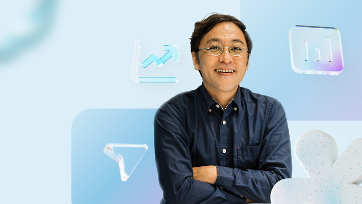 Man in glasses and a denim shirt smiling beside floating digital icons of graphs and data charts on a light blue background.