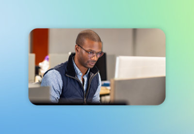 一位戴着眼镜、穿着背心的男士正在看着电脑屏幕。