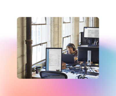 Una persona con auriculares se sienta en un escritorio con varios monitores de ordenador