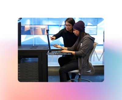 Dos personas trabajan juntas en un ordenador; una está sentada y tecleando, mientras que la otra está de pie