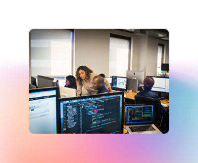 Varias personas trabajan en estaciones informáticas en una oficina. Dos personas están analizando el código de un monitor