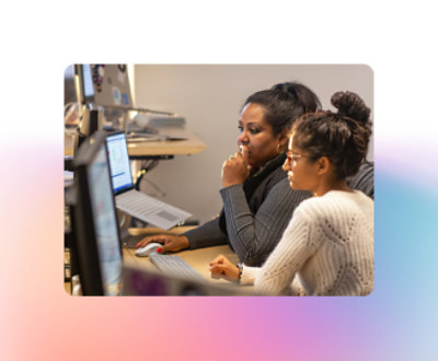 Dos mujeres concentradas en una pantalla de un ordenador en una oficina. Una teclea mientras la otra observa atentamente