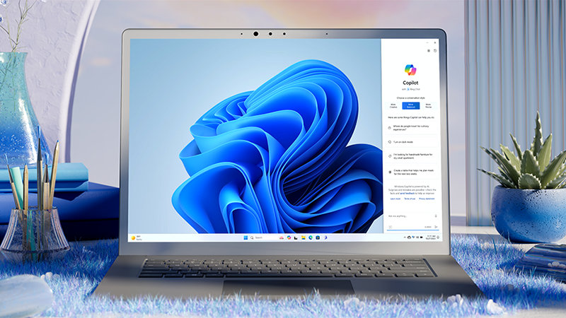 מחשב נייד עם תפרחת Windows 11 על המסך, מונח על משטח בצבע תכלת