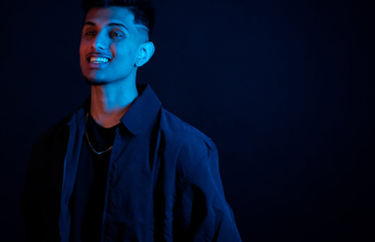 Muhammed Saif standing against a dark background, illuminated by blue light