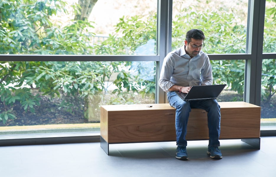 Uma pessoa sentada em um banco de madeira usando um laptop no colo.