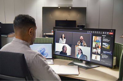 A person sitting in a chair participating in a Teams meeting being displayed on a large screen