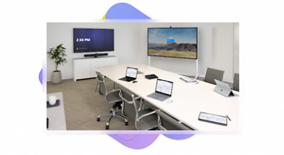 Teams console, laptops and tablets on a conference room table with two wall monitors..