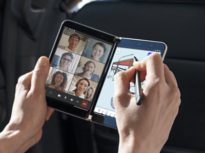 Sekelompok orang duduk di dekat meja dan menonton konferensi video di layar lebar.