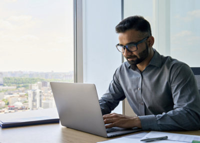 Uomo con gli occhiali, seduto in ufficio che lavora su un portatile