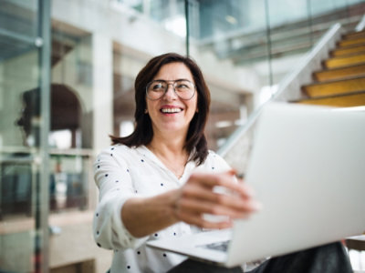 A woman wearing glasses and holding a laptop while smiling.