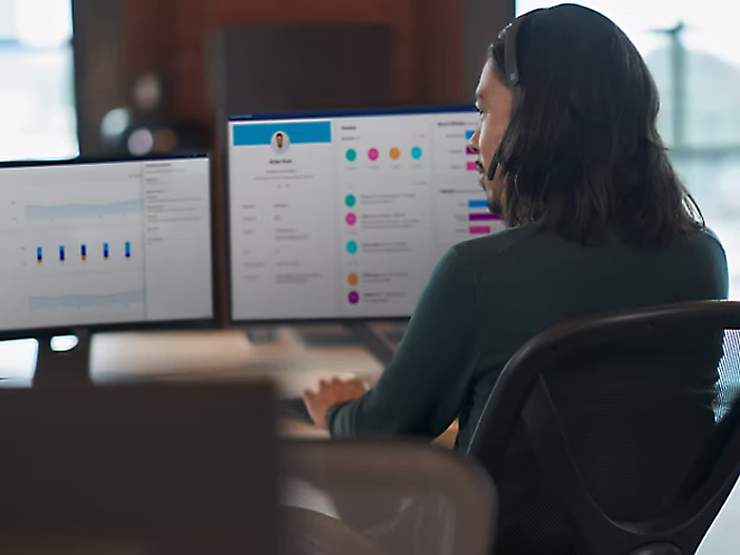 En person, der arbejder ved et skrivebord med to skærme, der viser grafer og projektstyringsværktøjer.