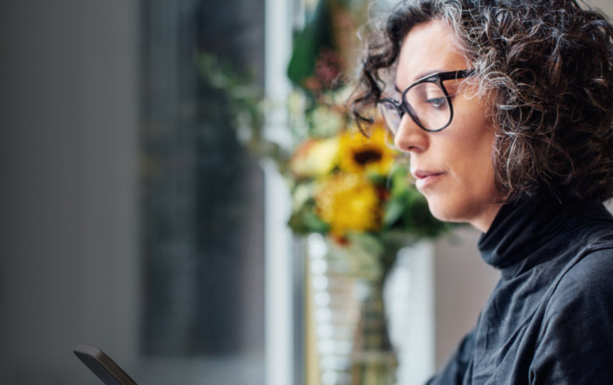 Mature businesswoman sitting, looking at her cell phone while working on laptop computer