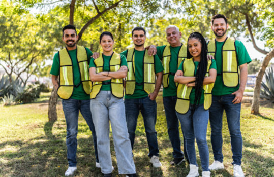 A group of nonprofit employees smiling in matching green shirts and yellow reflective vests 