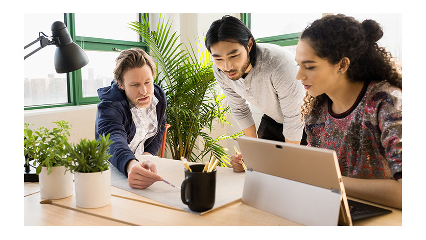 Three coworkers in an office setting working at a desk with a surface device