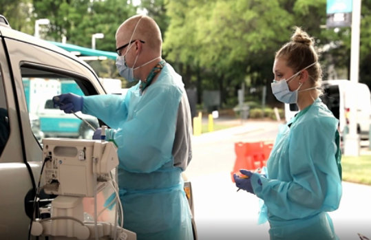 Twee personen in beschermende kleding die in een ambulance medische hulp verlenen