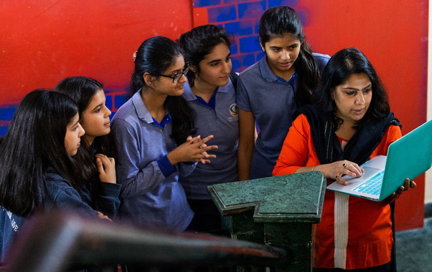 Een lerares geeft in een informele, kleurige omgeving een presentatie op haar laptop aan een aantal meisjes.