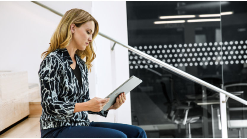 Eine Frau sitzt auf einer Treppe in einem Büro und liest auf ihrem Tablet.