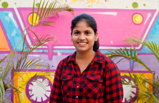 Young woman smiling standing in front of a colorful painted wall.