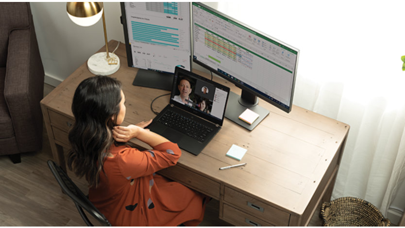 Une femme face à un ordinateur portable et deux moniteurs assistant à une réunion Microsoft Teams à la maison.