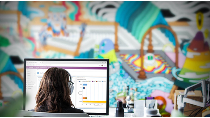 Een vrouw met een Surface-headset werkt op een monitor met kleurrijke kunst op de achtergrond.