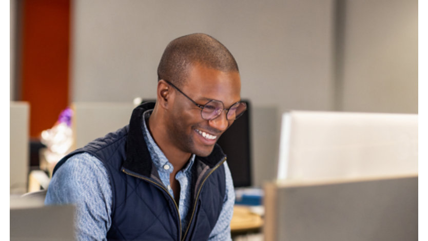 En person i et åbent kontormiljø smiler til en computerskærm.