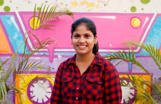 Ung kvinne som står smilende foran en fargerik malt vegg.