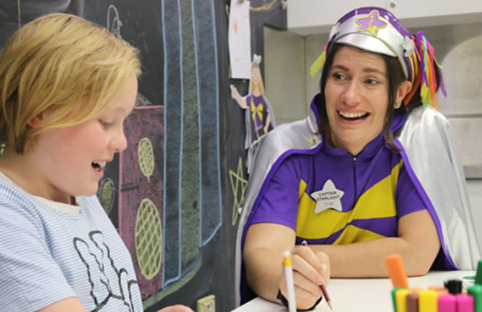 En voksen frivillig iført et kostume arbejder på et kunstprojekt sammen med et barn.
